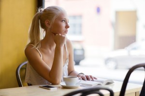 Pensive young woman at cafe looks out the window